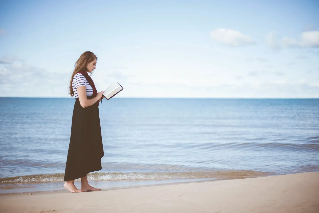woman reading bible walking on beach