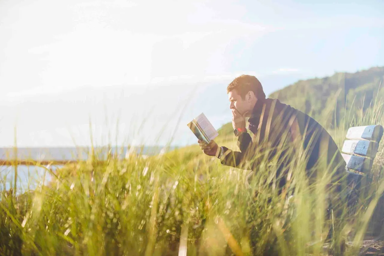 man in grass field reading Bible — Bible verse about restoration