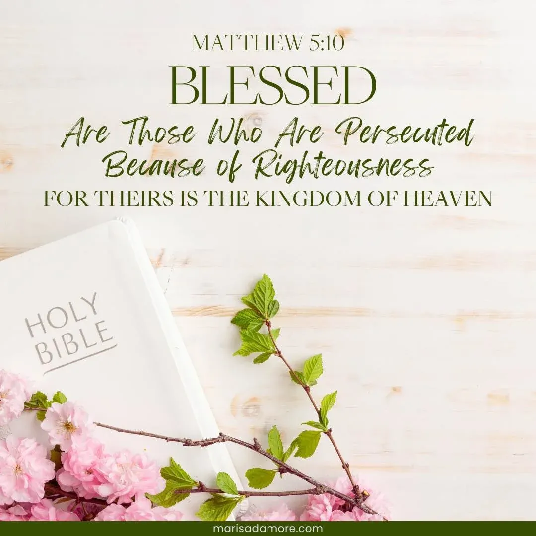 Pink flowers on top of a white Bible set on wood tabletop with image text Matthew 5:10 Blessed Are Those Who Are Persecuted