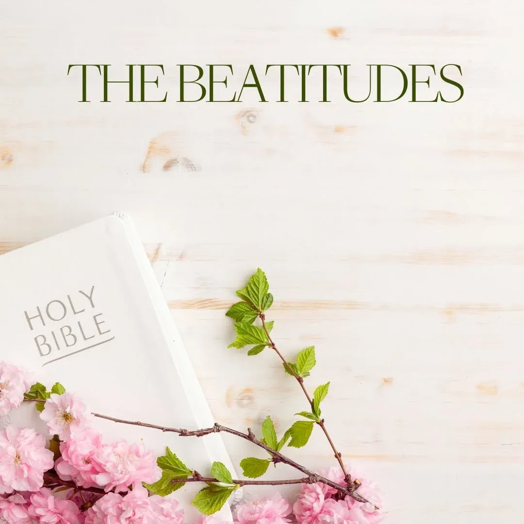 Pink flowers on top of a white Bible set on wood tabletop with image text The Beatitudes